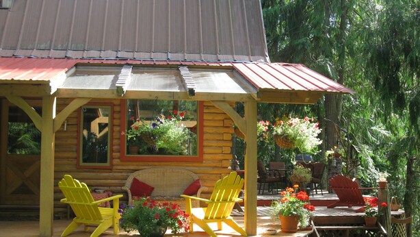 A wooden cabin with a porch, yellow Adirondack chairs, and potted plants. - Kaslo Getaway - private and natural experience. (Kaslo)