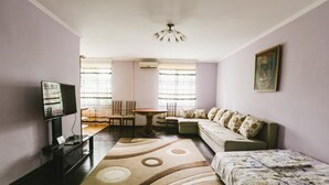 Ein Wohnzimmer mit einer Couch, einem Couchtisch, einem Fernseher und einem Essbereich mit Stühlen und einem Tisch.