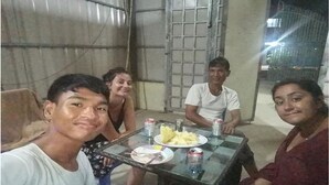 A group of people seated around a glass table with plates of food and drinks. - The Happy Family House (Angkor Borei)