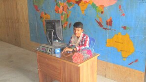 A person sitting at a desk with a computer and a map of the world on the wall behind them. - The Happy Family House (Angkor Borei)