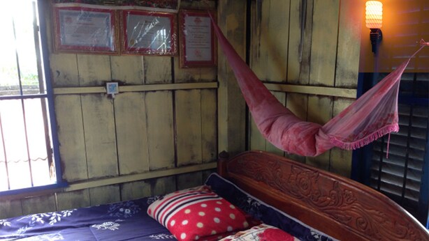 A bed with a floral-patterned bedspread, a wooden headboard, and a red and white polka-dotted pillow. - The Happy Family House (Angkor Borei)