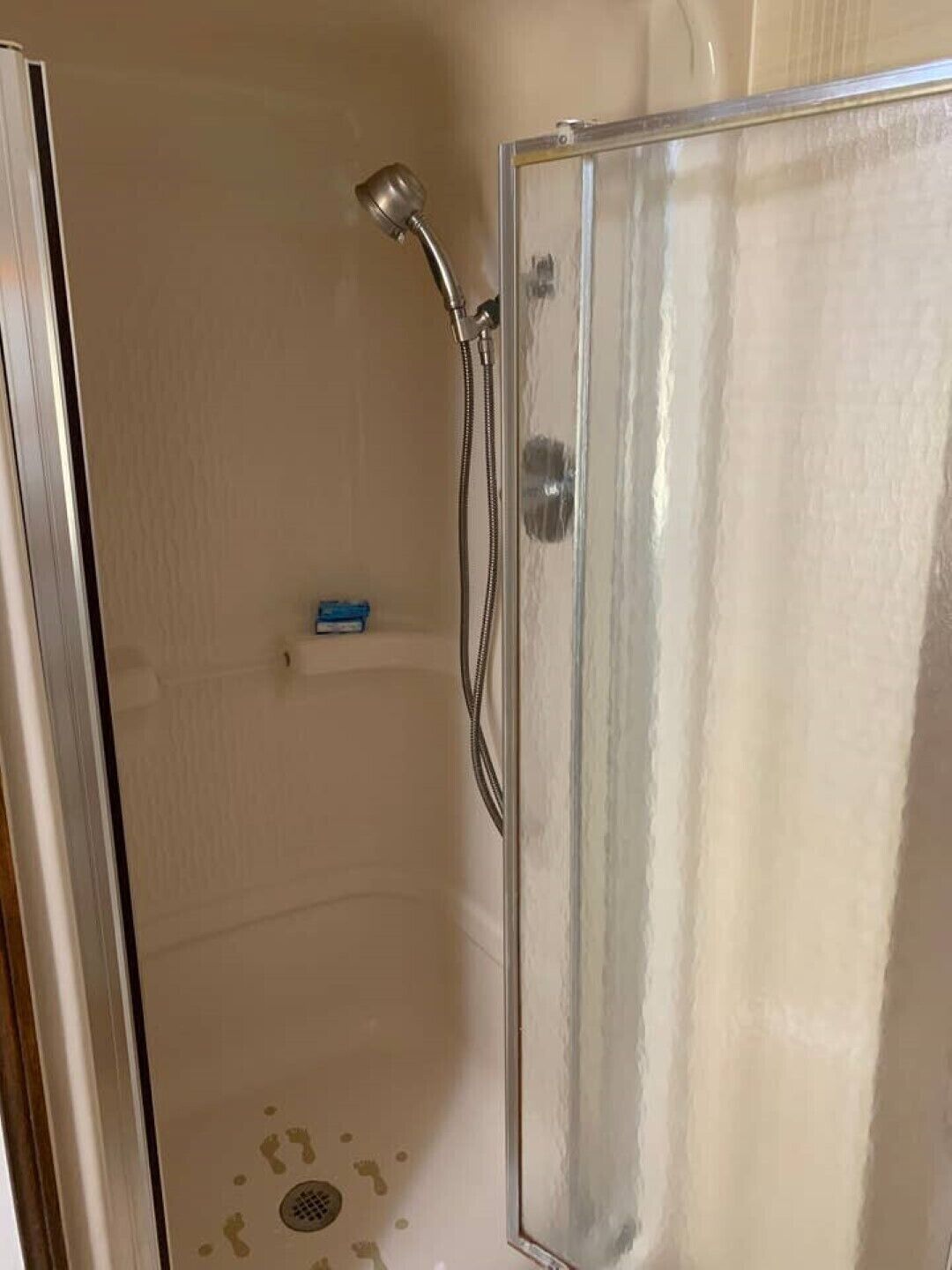 A shower with a glass door, a handheld showerhead, and a drain.