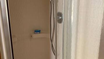 A shower with a glass door, a handheld showerhead, and a drain.