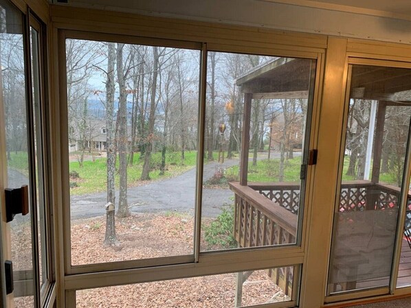 A view from a screened porch with a wooden deck and a covered area, overlooking a driveway and a wooded area with leaf-covered ground. - QUIET PRIVATE BLUFF TOP HIDEAWAY, CLOSE TO EVERYTHING (Guntersville)