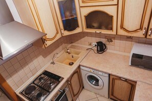 Compact kitchen with gas stove, oven, sink, and front-loading washing machine.