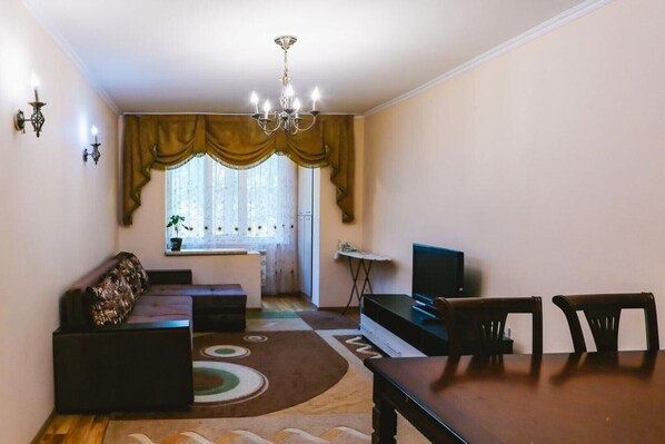 Cozy living space with a sofa, dining table, and TV, complete with a chandelier and potted plant.