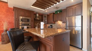 A modern kitchen with granite countertops, stainless steel appliances, and dark wooden cabinets.