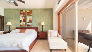 A bedroom with a bed, two nightstands, a chair, a large window, and a sliding glass door leading to a balcony.