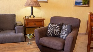 A cozy living room with a brown armchair, a wooden side table, a lamp, and a framed picture on the wall. - Princesa Resort E-408 Relaxation Clean Great Ocean Front Condo (Puerto Peñasco)