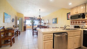 A kitchen with a central island, stainless steel appliances, wooden cabinets, and a dining area with chairs and a table. - Princesa Resort E-408 Relaxation Clean Great Ocean Front Condo (Puerto Peñasco)