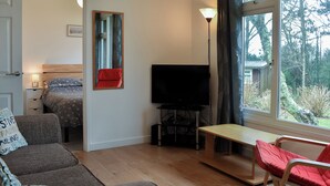A room with a bed, a TV, a sofa, a table, and a window with a view of trees. - 2 bedroom accommodation in Mount Hawke, near Redruth (Mount Hawke, near Redruth)