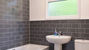 A bathroom with a bathtub, sink, and toilet against a tiled wall. - 2 bedroom accommodation in Mount Hawke, near Redruth (Mount Hawke, near Redruth)