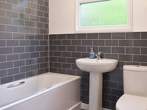 A bathroom with a bathtub, sink, and toilet against a tiled wall. - 2 bedroom accommodation in Mount Hawke, near Redruth (Mount Hawke, near Redruth)