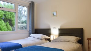 A bedroom with two single beds, a window with curtains, a bedside lamp, and a small picture on the wall. - 2 bedroom accommodation in Mount Hawke, near Redruth (Mount Hawke, near Redruth)