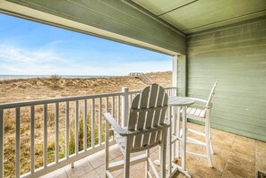Ein Balkon mit Blick auf den Strand, ein Stuhl und ein kleiner Tisch.
