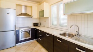 Eine moderne Küche mit Kühlschrank, Backofen und Mikrowelle aus Edelstahl. Ein Spülbecken mit Armatur, die Schränke sind dunkel.