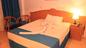 A neatly made bed with a white and blue bedspread, a wooden headboard, and a bedside table with a lamp and phone. - 100 Night per year at Grand Blue Hotels (Cairo)