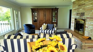 Una sala de estar con sofás a rayas, un sillón azul, una chimenea y un ventanal grande.