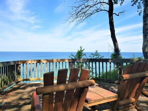 Eine Holzterrasse mit Blick auf das Meer, ausgestattet mit einer Holzbank und einem Baum.