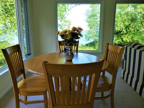 A dining area with a round wooden table, four wooden chairs, and a vase with flowers.