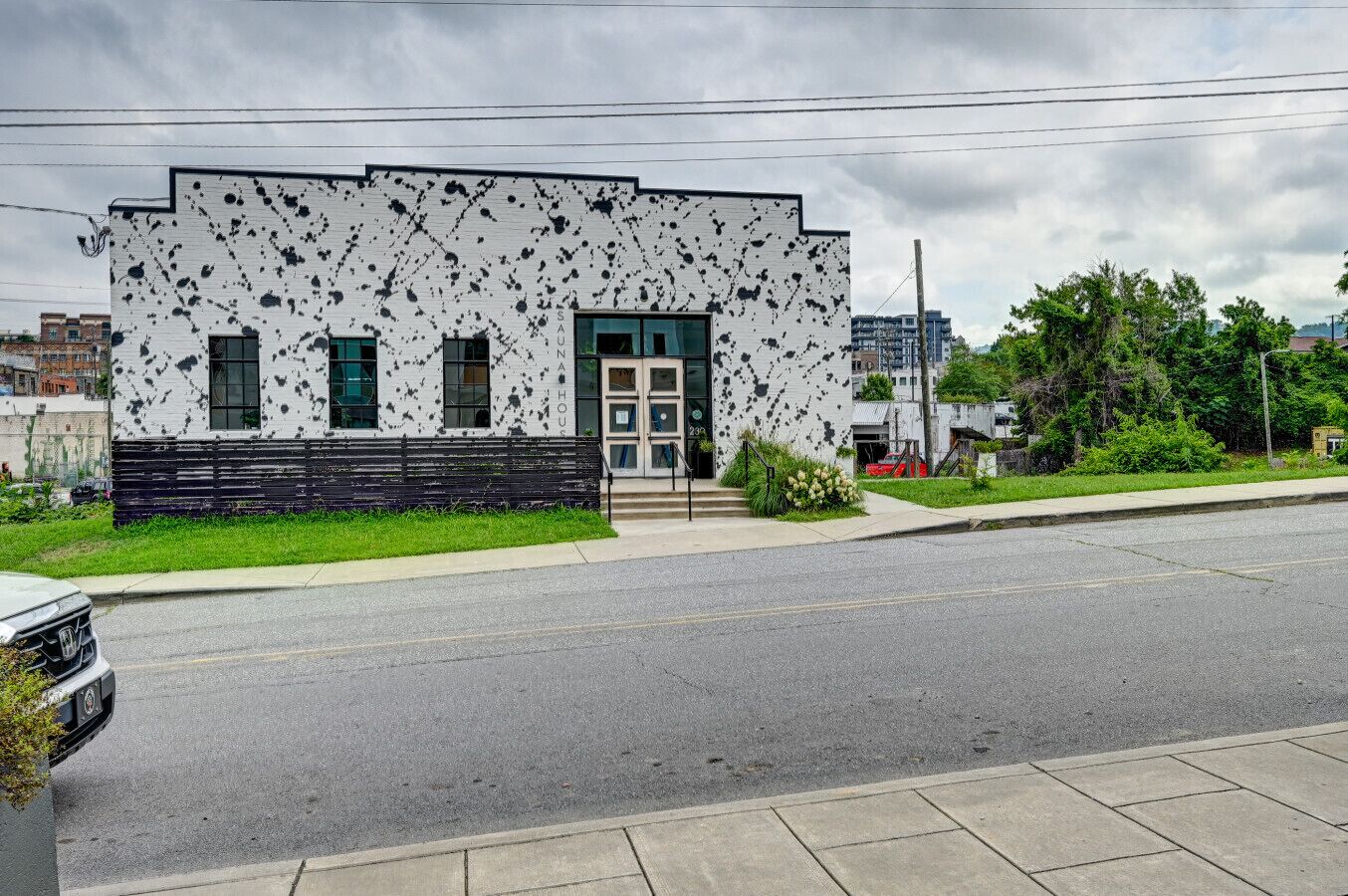 A modern building with a white facade and black speckles, a green door, and a small entrance with steps.
