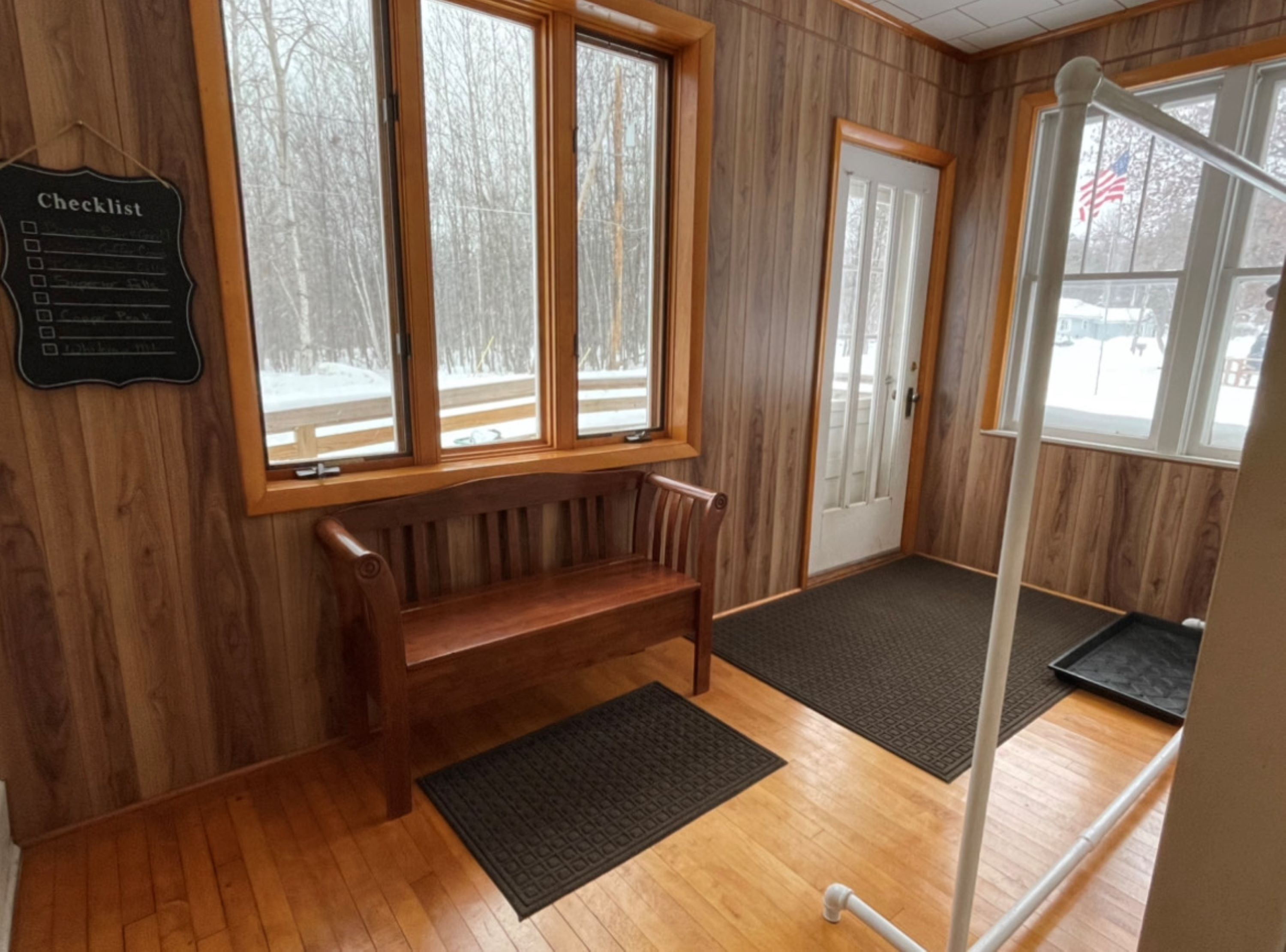 A room with a wooden bench, a door, and a window with a view of a snowy landscape.