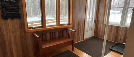 A room with a wooden bench, a door, and a window with a view of a snowy landscape.