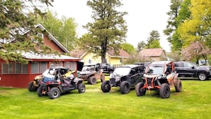 A row of off-road vehicles parked on a grassy area with houses in the background. - Close to Hurley, Trail access, near The Gile Flowage with Central Air & King Bed (Montreal)