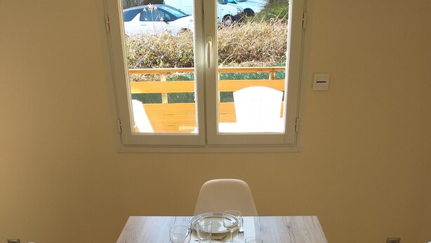 Ett matbord dukat med tallrikar, glas och bestick, med utsikt över en trädgård och parkerade bilar genom ett fönster.