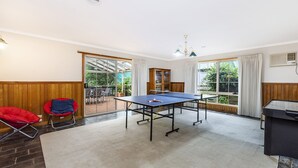 A room with a ping pong table, a red chair, a bookshelf, and a view of the outdoors through large windows. - Ideal family holiday home in the seaside town of Warrnambool (WARRNAMBOOL)