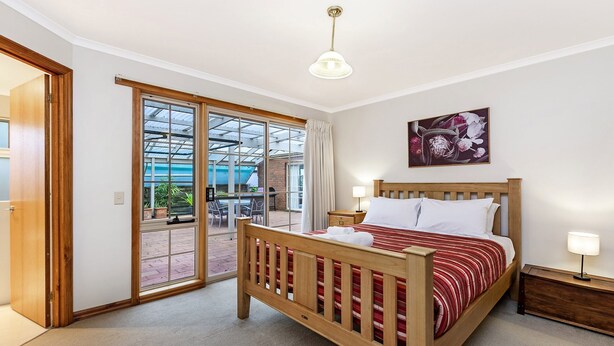 A hotel room with a wooden bed, a large window, and a ceiling light. - Ideal family holiday home in the seaside town of Warrnambool (WARRNAMBOOL)