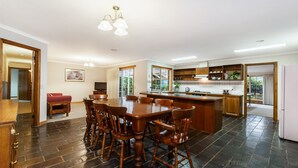 A spacious kitchen with a central island, wooden dining table, and chairs. There is a television and a painting on the wall. - Ideal family holiday home in the seaside town of Warrnambool (WARRNAMBOOL)