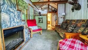 Een gezellige woonkamer met een stenen muur, een rode fauteuil, een gestreept bankstel en een aan de wand bevestigd moesshoofd.