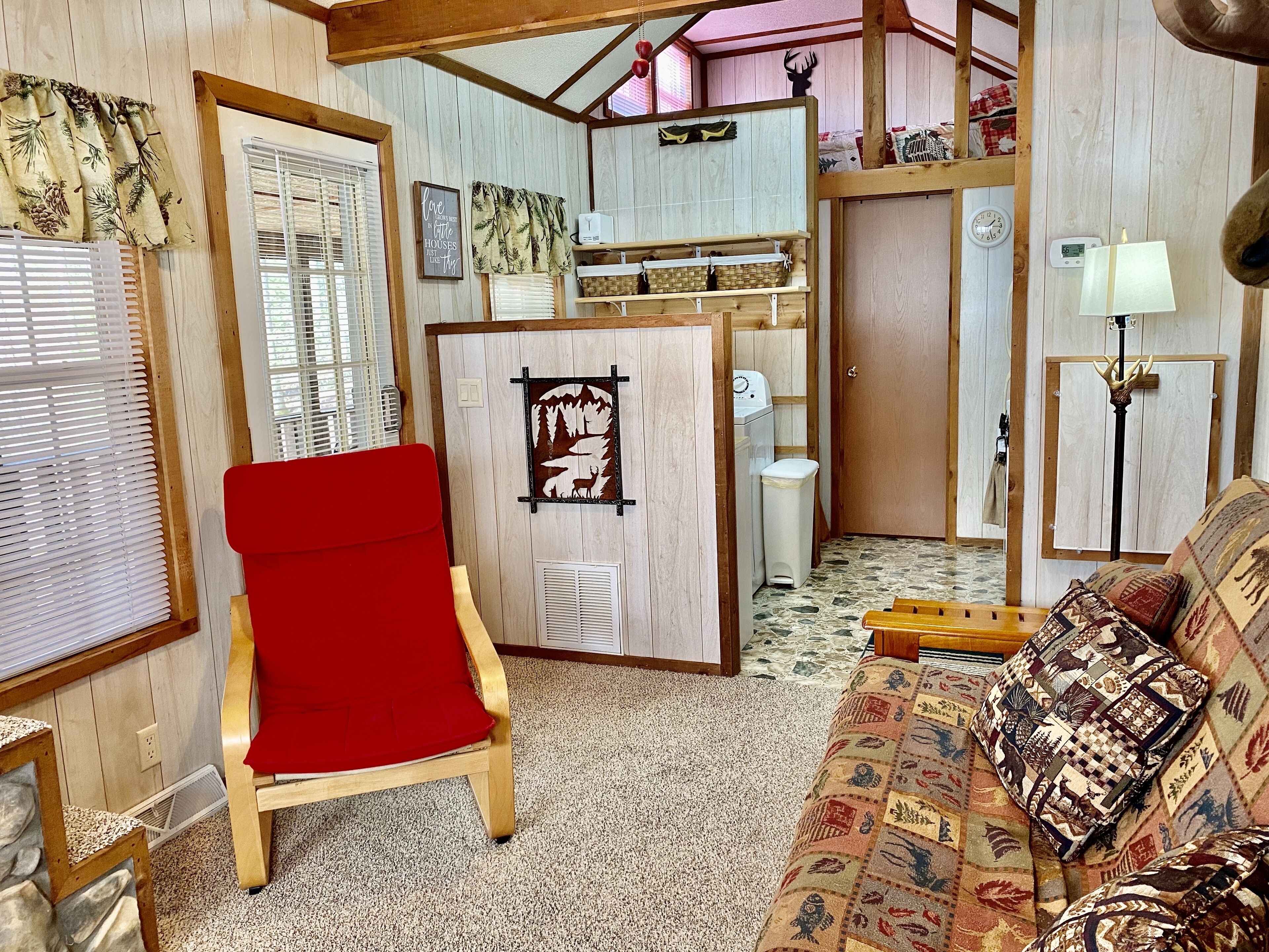 Uma sala de estar acolhedora com uma poltrona vermelha, um sofá estampado e teto de madeira.