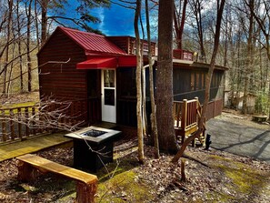 A small cabin with a red roof, a wooden deck, and a fire pit. - “Porch and Pine” not-so-tiny Tiny Log Cabin (Cosby)