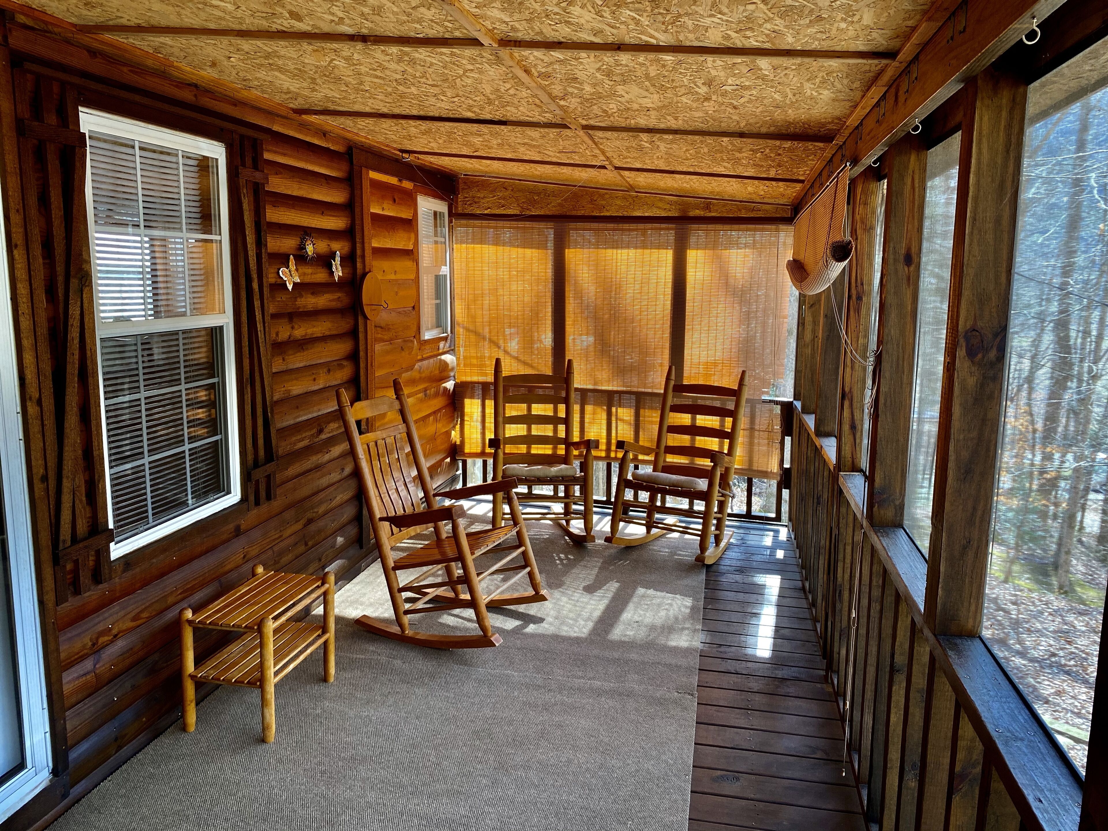 Une cabane en bois avec une véranda, des fauteuils à bascule et une table.