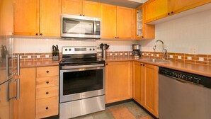 A kitchen with wooden cabinets, a stainless steel oven, a microwave, a dishwasher, and a sink. - 90 Glaciers Reach, this 2br home has a hot tub & pool in Whistler Village (Whistler)