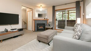 A living room with a fireplace, a television, and a sofa. - 90 Glaciers Reach, this 2br home has a hot tub & pool in Whistler Village (Whistler)