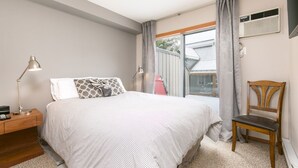A bedroom with a bed, a nightstand, a lamp, a chair, and a window with curtains. - 90 Glaciers Reach, this 2br home has a hot tub & pool in Whistler Village (Whistler)