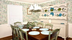 A dining room with a wooden table, six chairs, a chandelier, a wall-mounted plate rack, and a window with blinds.
