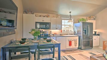 A modern kitchen with white cabinets, a stainless steel refrigerator, and a dining table set with bowls and glasses.