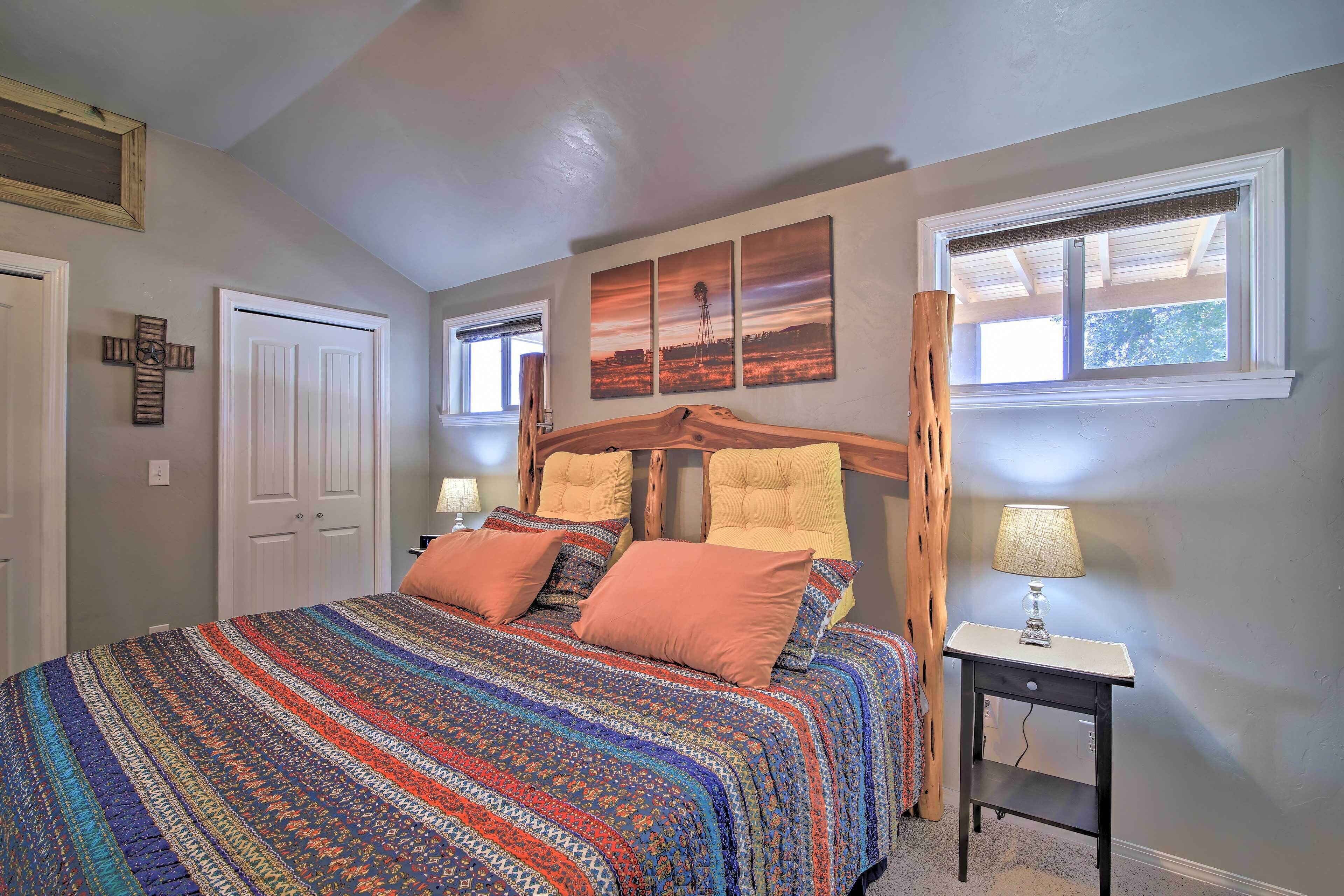 Une chambre à coucher avec un lit en bois, une couvre-lit à motifs, une table de chevet avec une lampe et une fenêtre donnant sur un paysage.