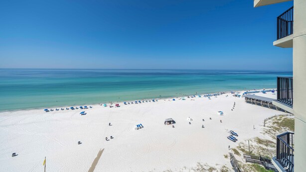 A beach view from a balcony with a clear sky, a sandy beach, and a few umbrellas and beach chairs. - Beach Front Condo with Endless Gulf Views!   (Panama City Beach)