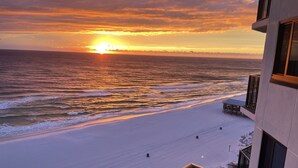 A beach view with a sunset, a building with a balcony, and a sandy shoreline. - Beach Front Condo with Endless Gulf Views!   (Panama City Beach)