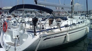 A white yacht named "BAVARIA" docked at a marina with other boats, featuring a covered deck area and life preserver visible.