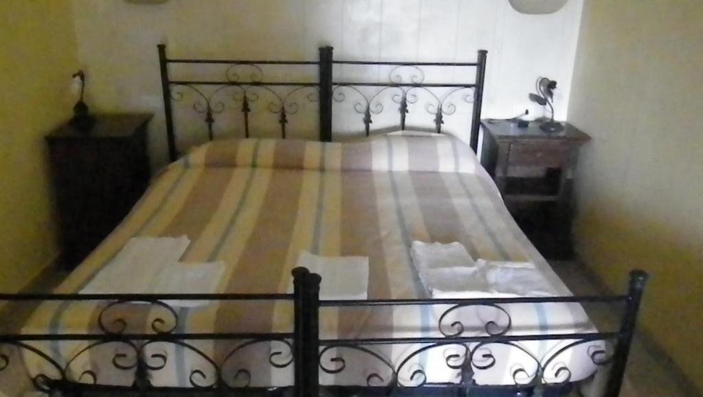 Een bed met een gestreept dekbedovertrek en kussens, een zwart metalen hoofdbord en een klein nachtkastje met een lamp.