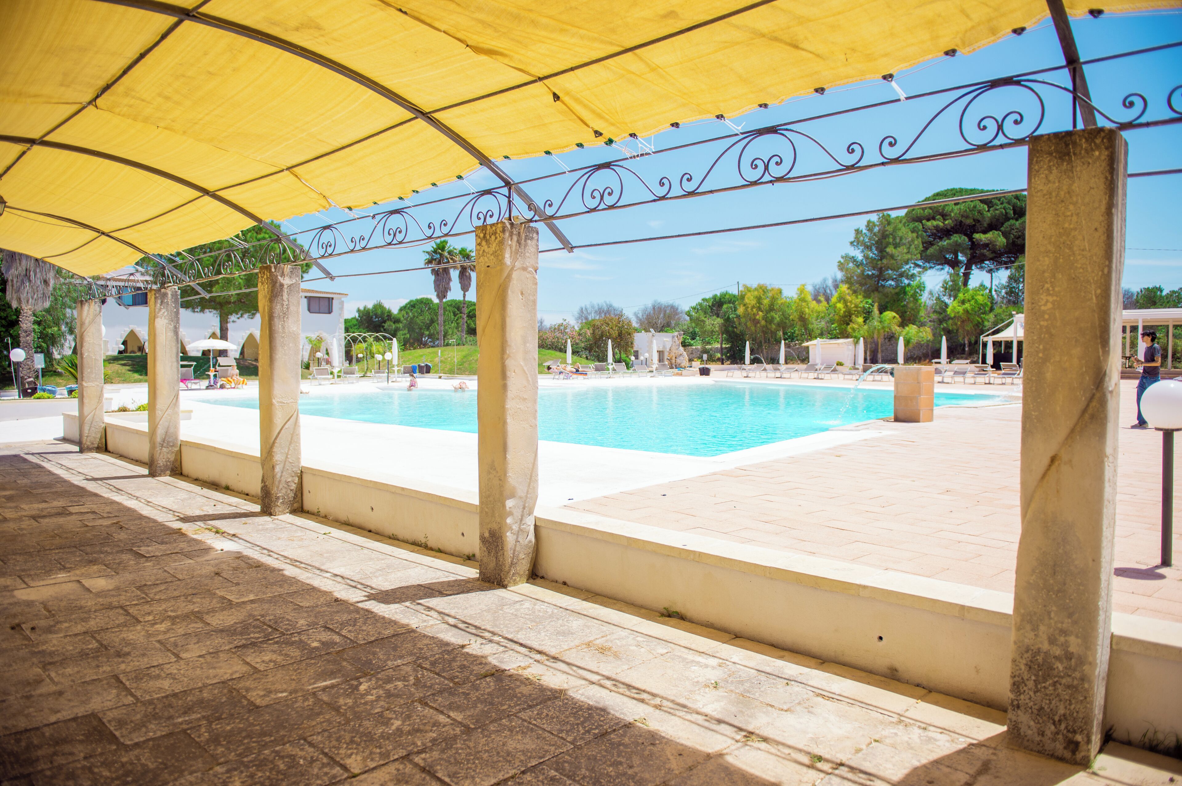 A pool area with a yellow canopy, stone columns, and a clear blue pool.