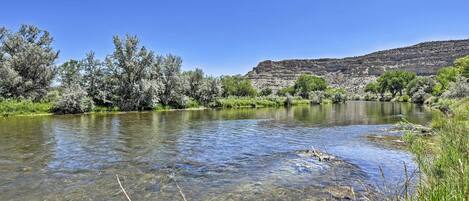 A clear river with surrounding vegetation and a hill in the background.