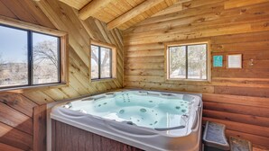 Eine Holzhütte mit Whirlpool, großen Fenstern und einer Holzbalkendecke.