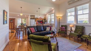 A spacious living area with a leather sofa, green armchairs, wooden flooring, and large windows providing natural light. - Lucy's Cottage in beautiful Kyneton (Kyneton)